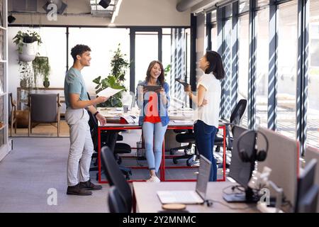Discussing project details, diverse colleagues using digital tablets in modern office setting Stock Photo
