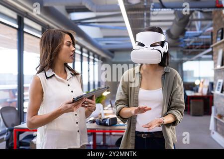 In office, Discussing design ideas, asian woman using VR headset while colleague holds tablet Stock Photo