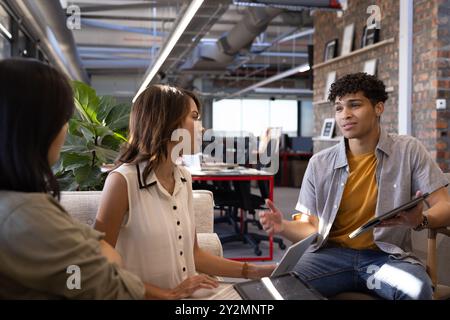Discussing project, diverse professionals collaborating with tablet and laptop in modern office Stock Photo