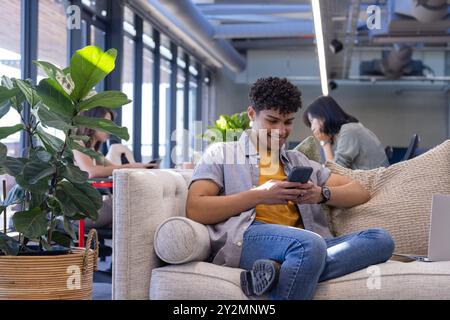 Using smartphone, man relaxing on couch in modern office space with plants Stock Photo