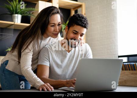 Happy interracial couple smiling while working or having fun at laptop Stock Photo