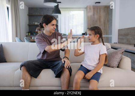 Teenage brother gave high five to his six year old sister after they finish and win game on console.  Stock Photo