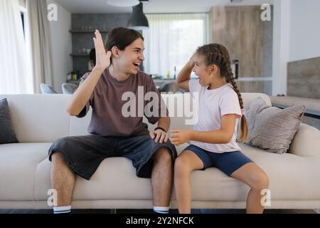 Teenage brother gave high five to his six year old sister after they finish and win game on console.  Stock Photo