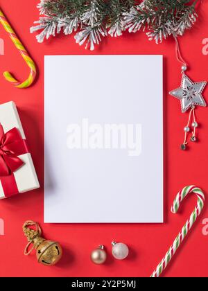 Blank white sheet and various Christmas decorations on red background, concept on the theme of letter to Santa Claus, template for designer Stock Photo