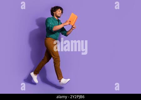 Photo of jumping young clever mexican university nerd man student in green shirt reading study materials isolated on violet color background Stock Photo
