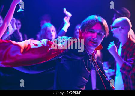 Group of young friends in Halloween costumes sharing laugh at party at nightclub, cheerfully dancing and having fun. Stock Photo