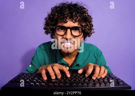 Closeup photo of arabian emotional aggressive guy working man look in pc screen using keyboard wear glasses isolated on violet color background Stock Photo