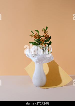 An elegant white vase adorned with delicate orange flowers on a soft beige background, accented by a subtle gold base Stock Photo