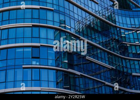Close-up view of a modern office building featuring a curved glass facade The blue tint and reflective surfaces highlight contemporary architectural e Stock Photo