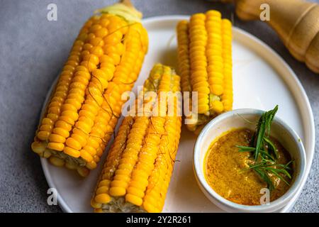 Fresh organic corn boiled to perfection, displayed on a white plate accompanied by a mustard sauce infused with tarragon herbs Stock Photo