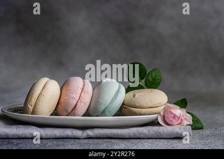 A collection of subtly colored macarons, delicately placed beside a blooming pink rose on a rustic grey background, embodying a serene and elegant aes Stock Photo
