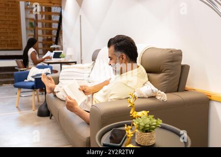 A serene scene of a middle-aged man comfortably reading on a recliner and a woman busy at a desk, representing a peaceful moment in a tastefully decor Stock Photo