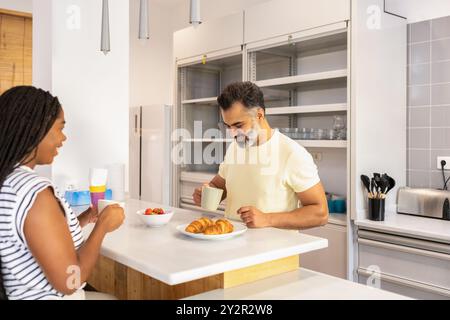A black woman and an indian man are having a pleasant breakfast in a bright, modern kitchen, illustrating a cozy, homey atmosphere Stock Photo