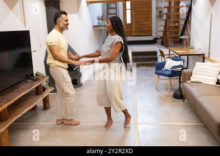 A joyful African American woman and her partner dancing in their stylish living room, sharing a warm, intimate moment in their cozy home Stock Photo