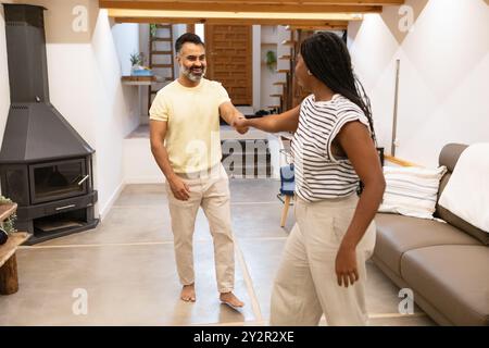 A Black woman smilingly shakes hands with an indian man in a modern, well-furnished living room, exemplifying warmth and elegant home life Stock Photo