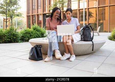 Two students working together on a laptop A student, with long braids, shows something to her classmate on the screen This image captures a typical sc Stock Photo