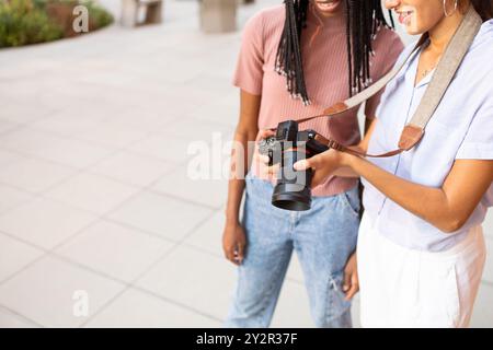 In the warm glow of a sunny campus, two vibrant university students, one holding a camera, are immersed in learning photography together, embodying a Stock Photo