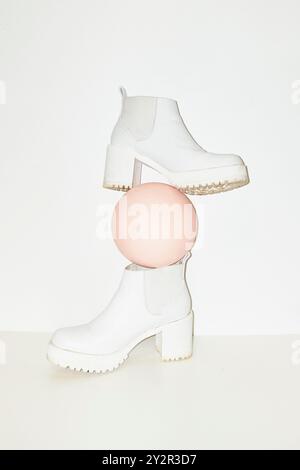 Elegant white platform boots paired with a soft pink geometric sphere, creating a contemporary and artistic fashion statement Stock Photo