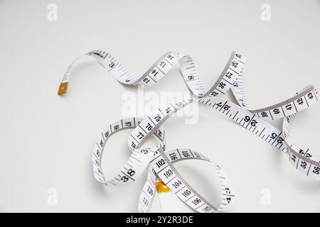 A simple, white measuring scale tape coils in a random, loosely arranged pattern against a stark white background, highlighting its black detailed mar Stock Photo