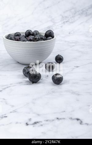 White ceramic bowl filled with juicy blueberries on a marble surface, depicting freshness and healthy ingredients. Stock Photo