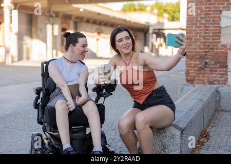 A heartwarming scene of two young women, one using a wheelchair, sharing a joyous moment together outdoors They are both smiling and engaged in captur Stock Photo