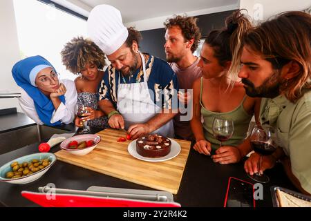 A group of diverse friends enjoys preparing food together in a stylish modern kitchen, with a man in chef's attire taking the lead Stock Photo
