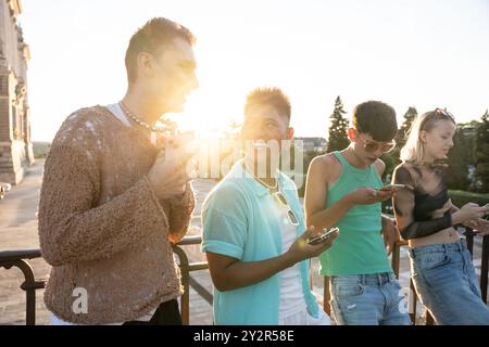 A diverse group of LGBTQIA+ friends smiling, chatting, and using smartphones while enjoying a sunny day outdoors. Stock Photo