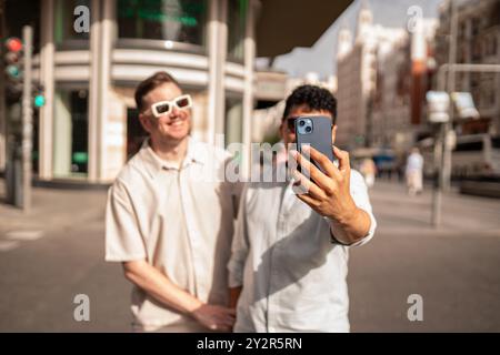 A delightful image capturing a multiethnic gay couple having fun in an urban setting, with one man taking a selfie while both smile brightly. Stock Photo