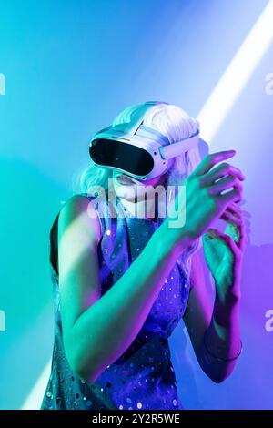 A striking image of a futuristic woman, fully immersed in a virtual reality experience. Her vividly illuminated surroundings, featuring intense hues o Stock Photo