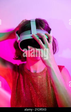 A woman explores virtual environments using a VR headset against a colorful neon background, symbolizing digital interaction in a futuristic scenario. Stock Photo