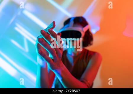 A woman wears a VR headset, displaying futuristic virtual reality interaction, against a vibrant, neon-lit background, symbolizing advanced digital ex Stock Photo