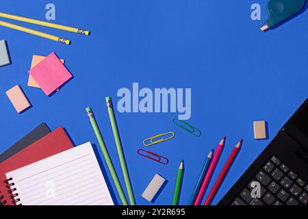 Top view of a vibrant selection of school supplies, including pencils, erasers, paper clips, and notebooks, neatly arranged on a bright blue backgroun Stock Photo