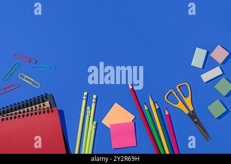 Top view of a vibrant assortment of school supplies, including pencils, scissors, and notebooks, set against a vivid blue background. This flat-lay ar Stock Photo