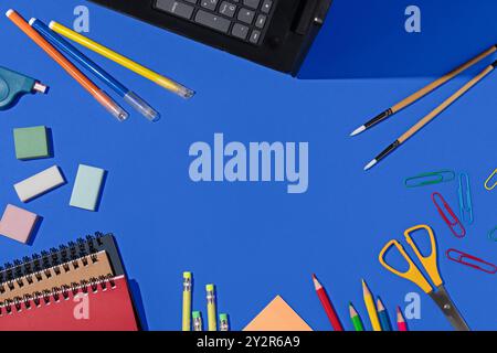 Top view of a vibrant selection of school supplies, including pencils, erasers, paper clips, and notebooks, neatly arranged on a bright blue backgroun Stock Photo
