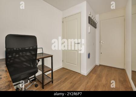 A and contemporary home office setup featuring a black office chair, wooden desk, and white walls. Stock Photo