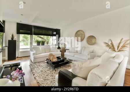 An elegant modern living room boasts white sofas, decorative pillows, a textured rug, and tasteful wall art, with natural light streaming in. Stock Photo