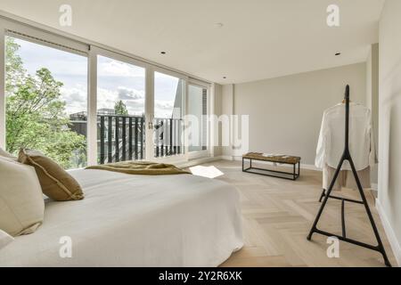 A spacious modern bedroom featuring large windows, balcony access, a comfortable bed, and wooden floor. Stock Photo