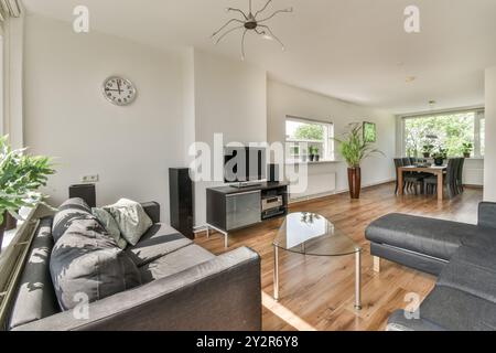 A spacious modern living room featuring a cozy sofa, a sleek TV stand, a glass coffee table, and a dining area bathed in natural light. Stock Photo