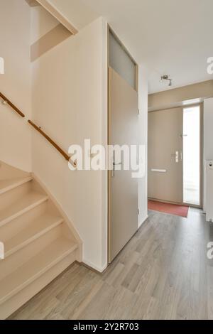 A well-lit modern home interior featuring a wooden staircase leading to an upper level and a contemporary white door in the hallway. Stock Photo