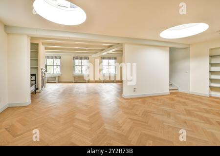 An expansive, unfurnished room featuring polished hardwood floors, large windows providing plenty of natural light, and built-in shelves. Stock Photo