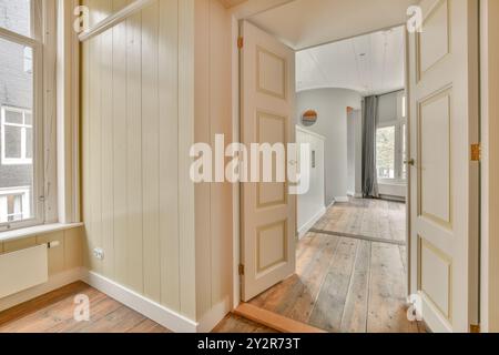 Warm and welcoming empty hallway in a house, featuring wooden floors, white walls, open doors, and a large bright window. Stock Photo