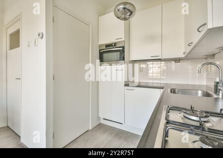 This image shows a bright and airy modern kitchen with white cabinetry, stainless steel appliances, and a glimpse of natural light coming in through t Stock Photo