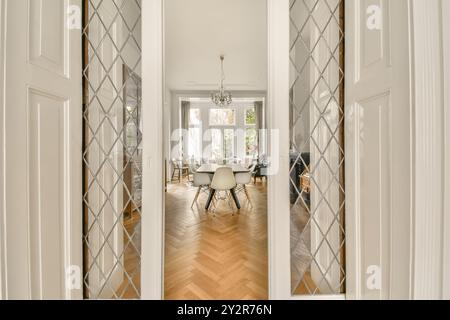 A luxurious dining room with a large table set seen through elegant, open French doors with glass panes set in a bright, spacious home. Stock Photo