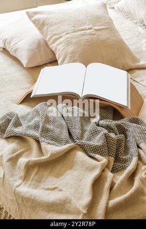 Open blank book laying on a bed with soft pillows and textured blanket, embodying a peaceful and cozy atmosphere ideal for relaxation. Stock Photo