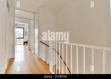 An empty well-lit corridor featuring wooden floors, white walls, and a simple stair banister in a contemporary house. Stock Photo