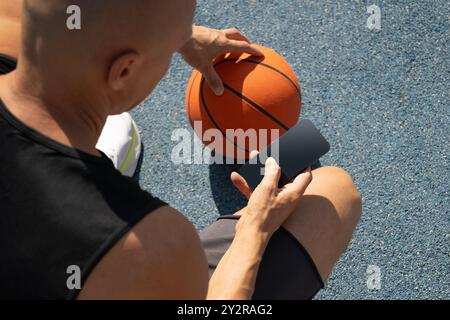 Basketball player using smartphone and texting social media during game interval, Outdoor training. View from above. Stock Photo