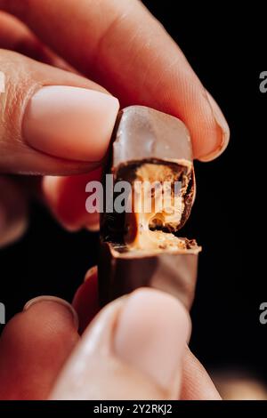 Close-up of fingers holding chocolate candy with caramel filling oozing out, dessert concept Stock Photo