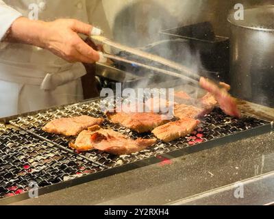Chef grilling beef steaks on a barbecue grill in a restaurant kitchen Stock Photo