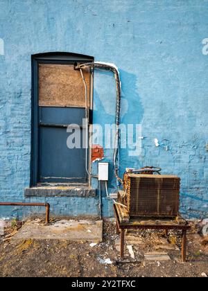 A rusty air conditioner is sitting on a table outside the boarded window of an abandoned building Stock Photo