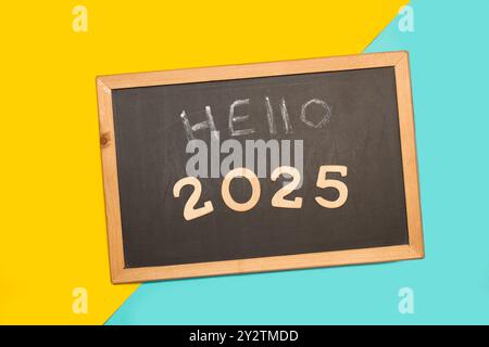 Hello 2025 short phrase on a blackboard on a light blue and yellow background Stock Photo